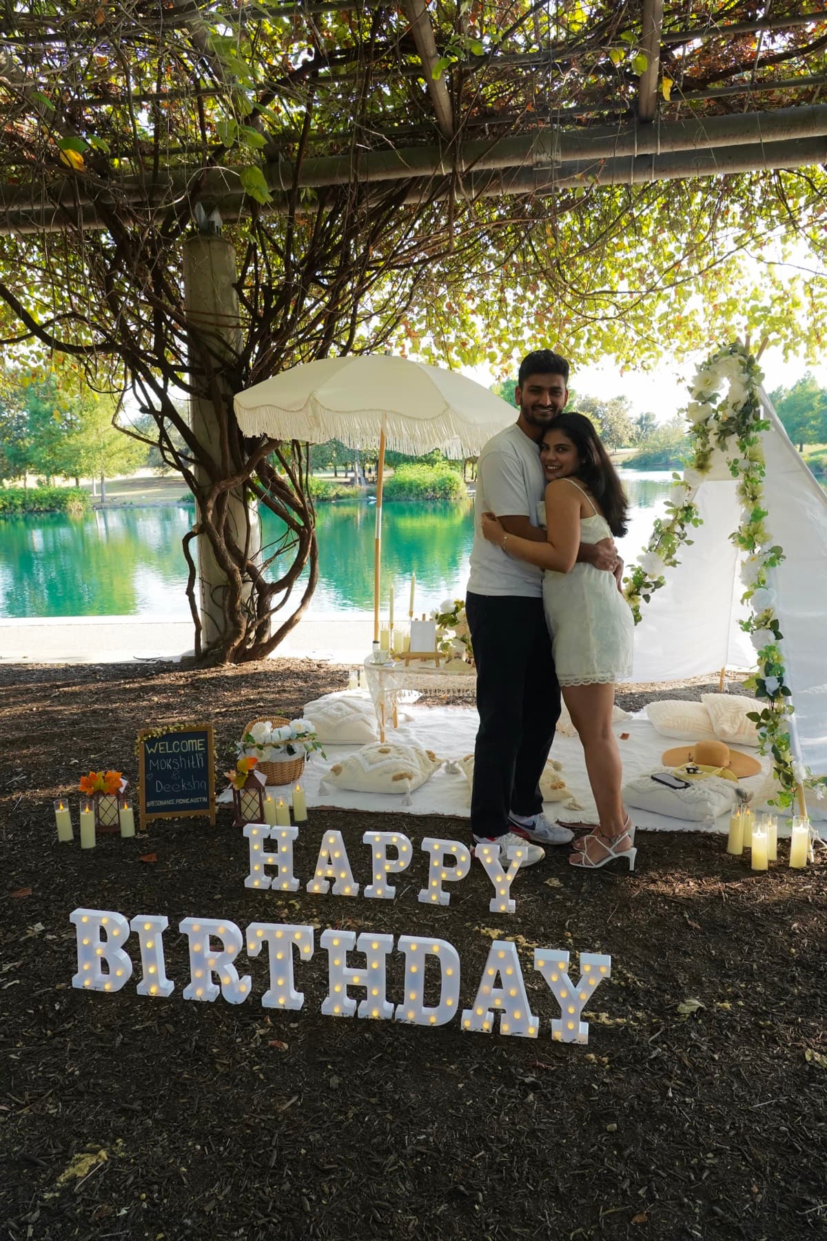 Couple hugging at their birthday picnic with glowing letters in Austin