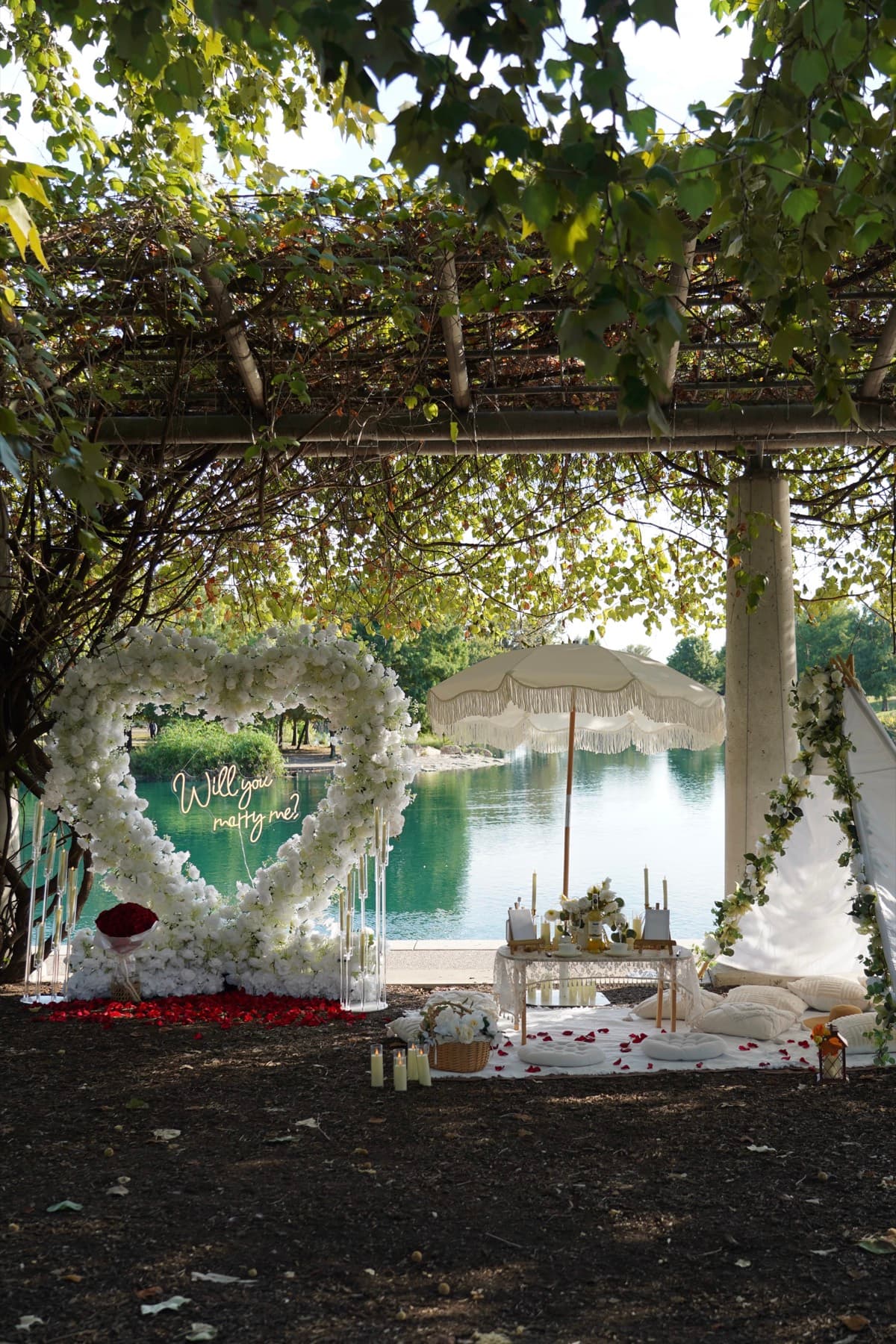 Proposal arch and picnic setup with a fringe umbrella by the lake in Austin