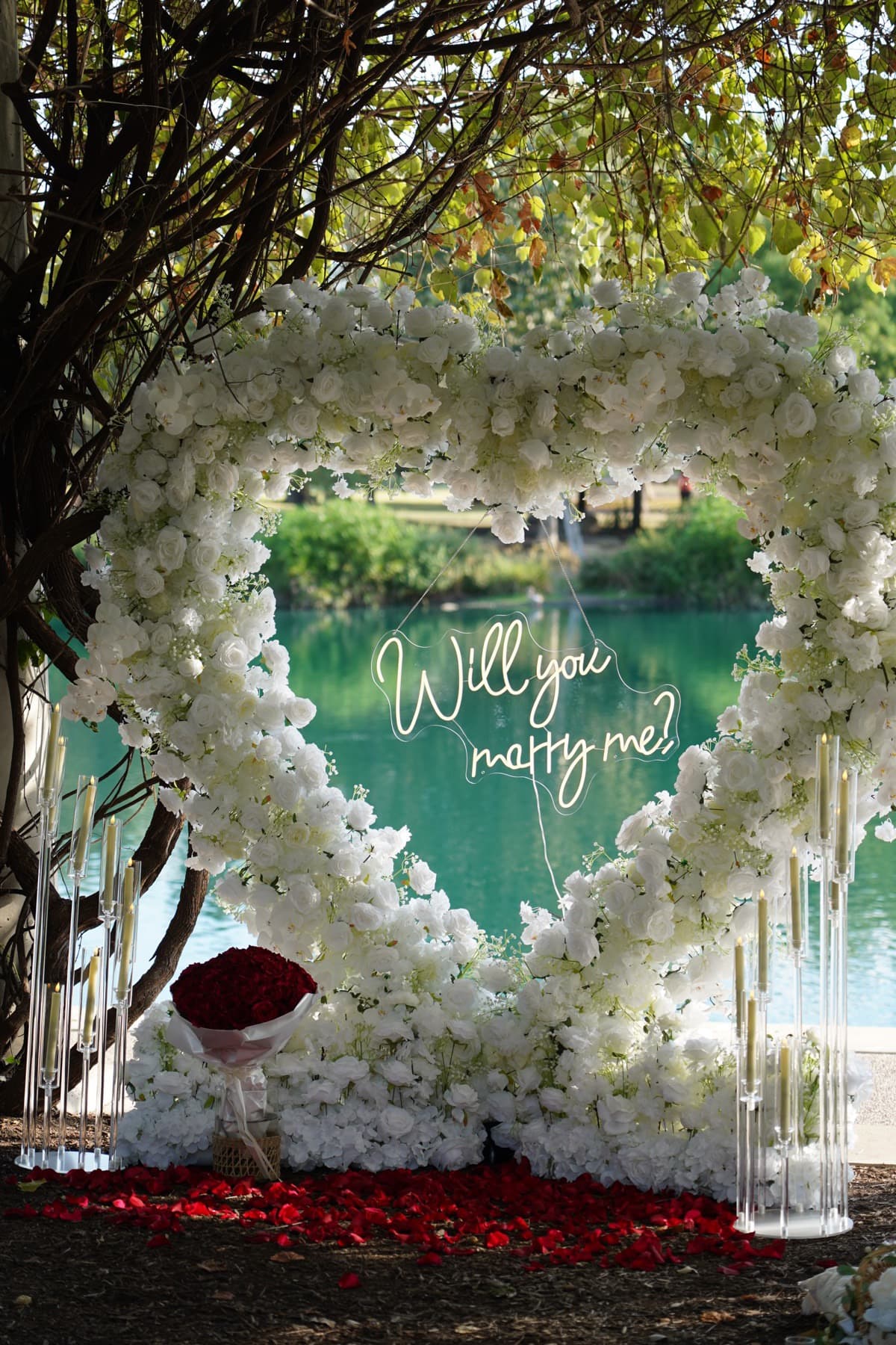 White rose heart arch with red rose bouquet and rose petals by the lake in Austin