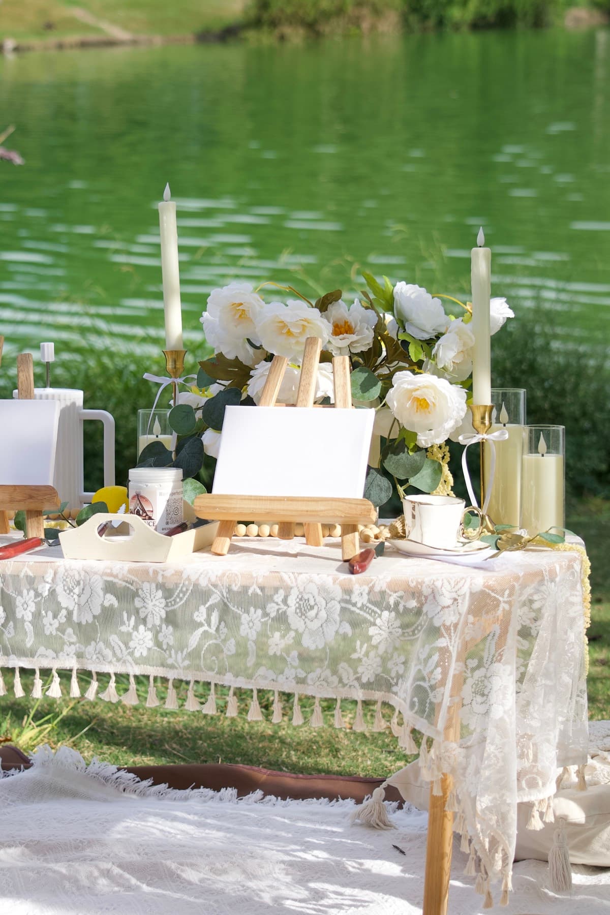 Mesa de pícnic elegante junto al lago con caballetes de pintura y peonías blancas en Austin