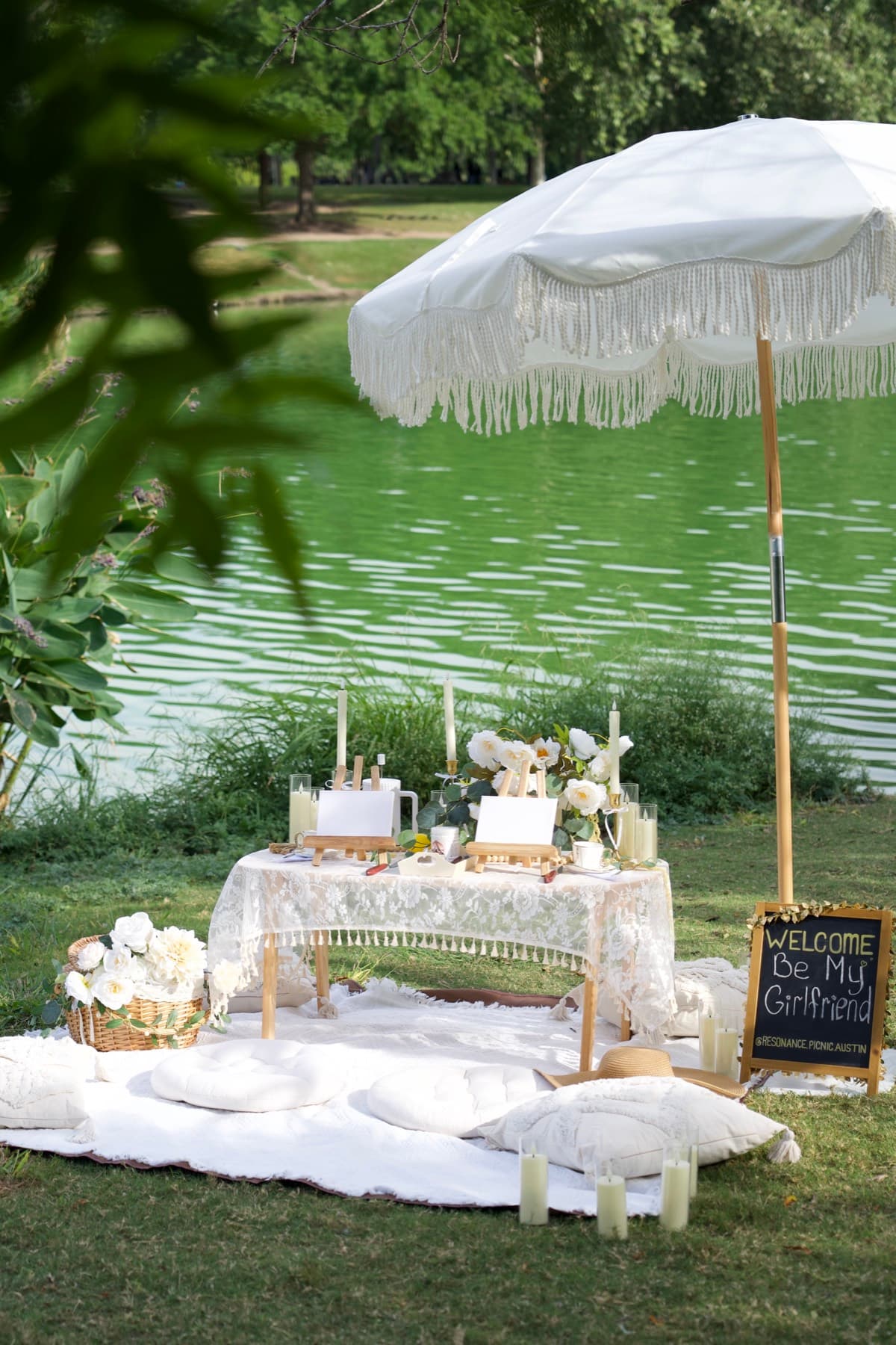 Pícnic romántico de pedida de mano junto al lago con sombrilla blanca de flecos en Austin