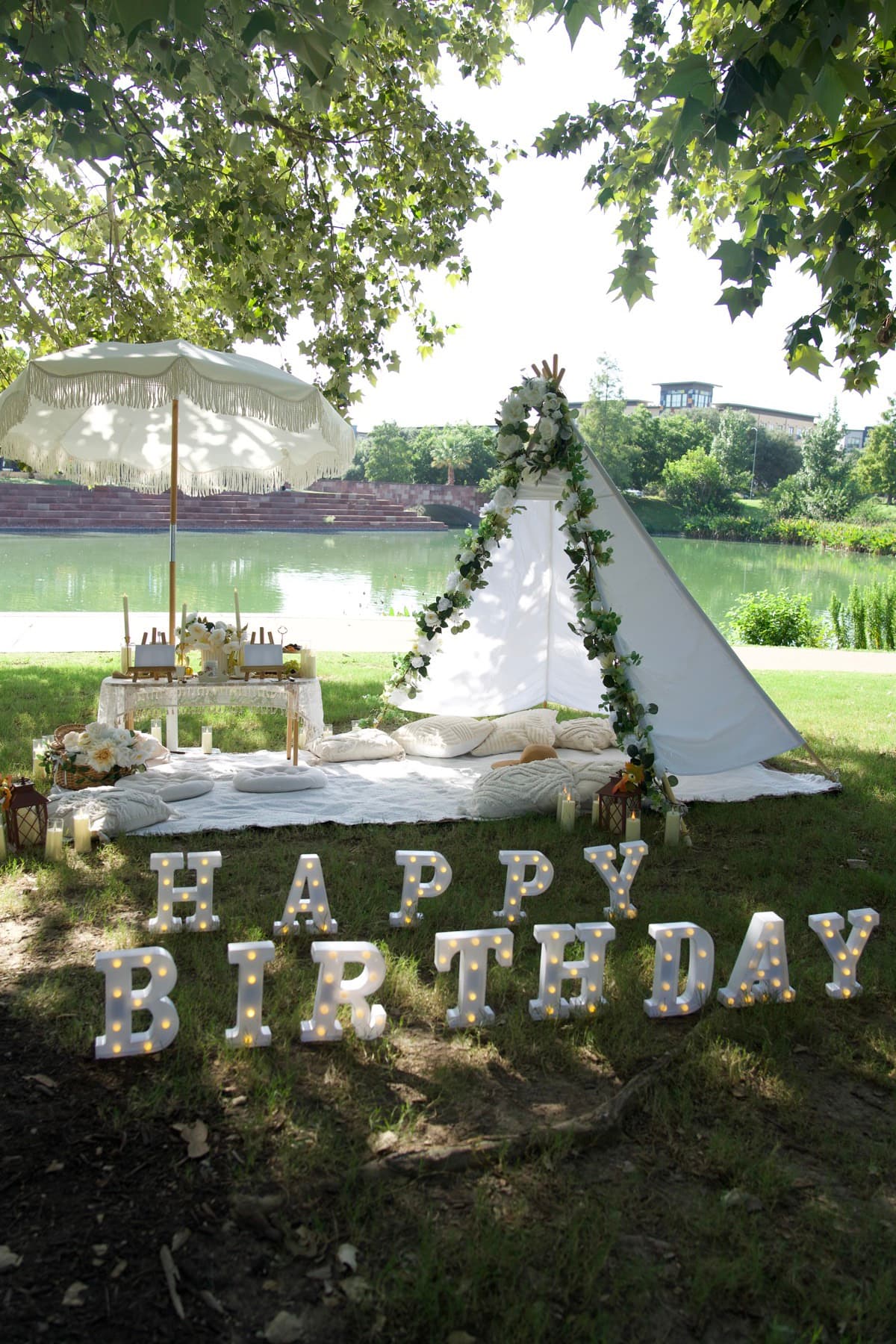 Montaje de pícnic de cumpleaños con carpa blanca, sombrilla de flecos y vistas al lago en Austin